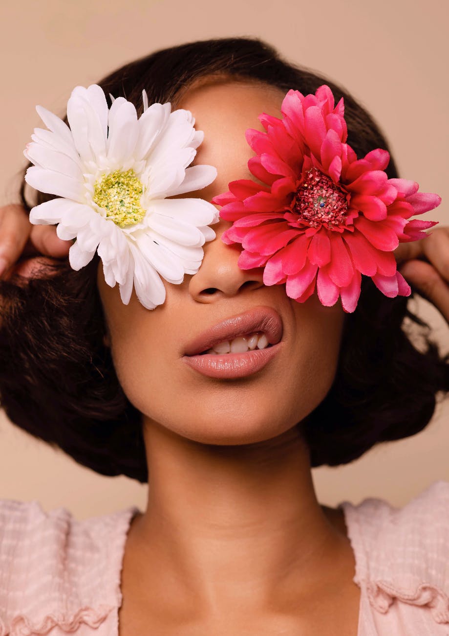 woman holding two flowers across her eyes